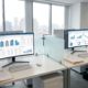 Twee digitale werkstations met vastgoedbeheer software en ERP dashboards in modern kantoor met huisvestingsdocumenten